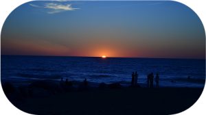 Coucher de soleil sur l'océan avec des silhouettes de personnes au premier plan.
